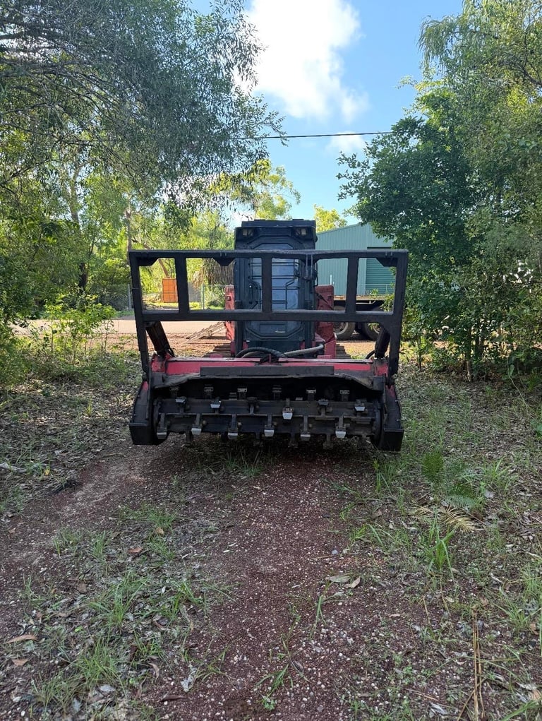 Rear view of industrial agricultural machinery on a dirt path surrounded by green trees and vegetation